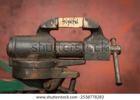 Concept of dealing with problem. Vice grip tool squeezing a plank with the word frightful