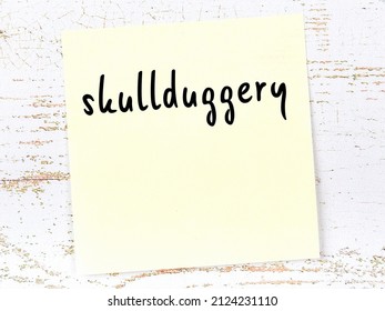 Concept of reminder about skullduggery. Yellow sticky sheet of paper on wooden wall with inscription