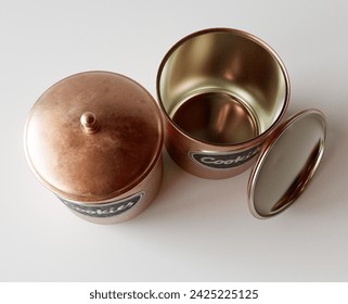 A concept showing two copper cookie jar tins with a metal embossed label on a white studio background - 3D