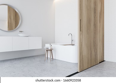 Corner Of Spacious Bathroom With White Walls, Stone Floor, Comfortable Bathtub And Sink Standing On White Countertop With Round Mirror And Sliding Door. 3d Rendering