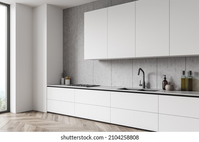 Corner View On Bright Kitchen Room Interior With Cupboard, Panoramic Window, Electric Cooker, White Wall, Sink, Liquid Soap And Oak Wooden Parquet Floor. Concept Of Minimalist Design. 3d Rendering