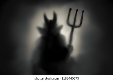 Creepy Devil silhouette behind a frozen glass and in the mist with backlit.