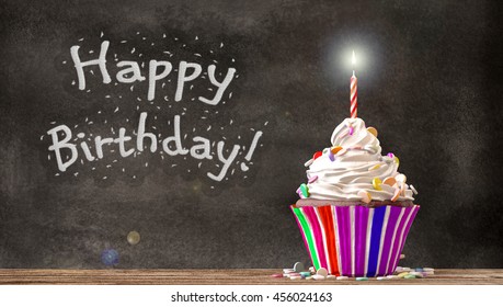 Cupcake With Cream, Candies And A Candle On A Wooden Table With Happy Birthday Written On A Blackboard Background. Empty Free Copy Space Available. 3D Rendering