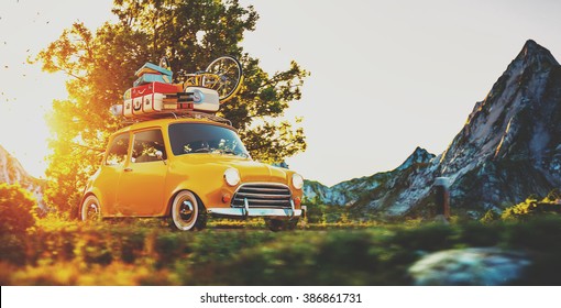 Cute little retro car with suitcases and bicycle on top goes by wonderful countryside road at sunset
