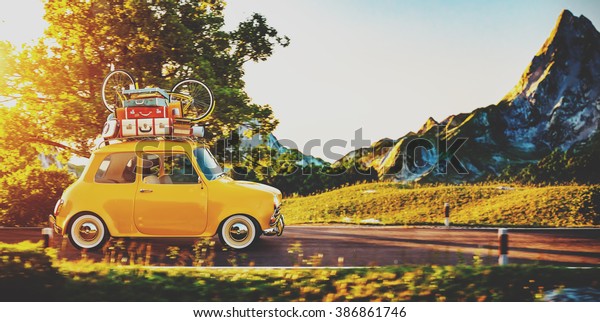 Cute little retro\
car with suitcases and bicycle on top goes by wonderful countryside\
road at sunset