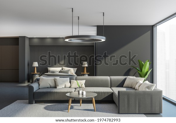 Dark bedroom interior with\
corner sofa and coffee table, grey carpet and concrete floor.\
Sleeping bed and window with city view. Mockup copy space blank\
wall, 3D rendering