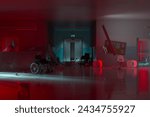 A decrepit hospital corridor bathed in sinister red light, strewn with rubble, abandoned furniture, and a lone overturned wheelchair paints a scene of post-calamity desolation.