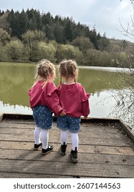 Description:
Two young children stand side by side on a wooden platform, looking out over a still lake surrounded by trees. Their matching outfits and close stance create a sweet, peaceful moment.

