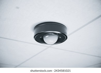 Detailed view of an advanced motion sensor mounted on the ceiling within a modern office setting, emphasizing its sleek and functional design for enhanced security.