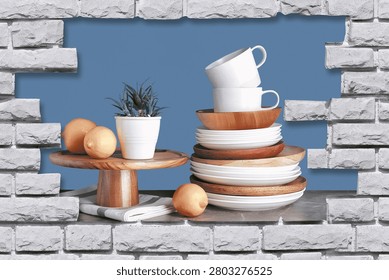 Digital kitchen wall tile design with a modern crockery and rustic wood theme.

The central artwork showcases a stack of ceramic plates and bowls mixed with natural wooden plates. Two cups are neatly stacked on top. To the left, a wooden cake stand holds fresh lemons and a small potted plant, with a folded napkin underneath. The setup is arranged against a clean steel-blue background.

The entire scene is framed by a realistic stone brick border with a 3D broken-wall effect, creating the illusion of a kitchen shelf built into the wall. The mix of ceramics, wood textures, and greenery gives a fresh, organic, and minimal vibe.

Glossy finish design ideal for kitchen backsplash, dining areas, cafes, and modern homes. High-resolution digital print for ceramic and vitrified wall tiles. The natural tones and clean styling add warmth and sophistication to contemporary interiors.