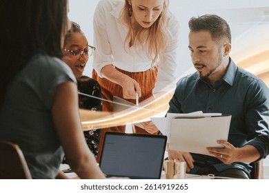Diverse group collaborating at a table with laptops and documents. Teamwork and discussion among colleagues in a modern office setting. Business meeting image. - Powered by Shutterstock - Get 15% off with code: PIKWIZARD15