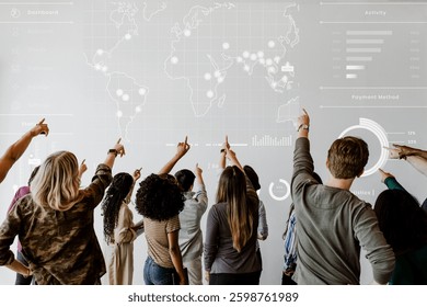 Diverse group of people pointing at a world map on a screen, analyzing data and graphs. Teamwork and collaboration in a modern office setting. Education and learning image.