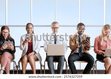 Diverse group of professionals using devices. Men and women of various ethnicities engaged with laptops and smartphones in a modern office setting. Business people working on digital devices.