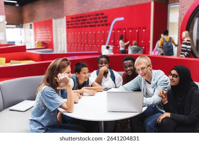 Diverse group of students studying together around a laptop in a modern school setting. Collaborative learning, teamwork, and education in a vibrant environment. Diverse students in school discussion. - Powered by Shutterstock - Get 15% off with code: PIKWIZARD15