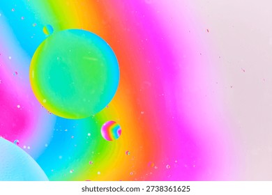 Dynamic macro photography featuring large green blue oil bubble and smaller rainbow colored bubble suspended in pink liquid environment