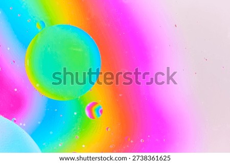 Dynamic macro photography featuring large green blue oil bubble and smaller rainbow colored bubble suspended in pink liquid environment
