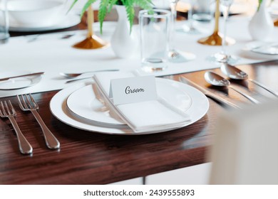 An elegantly styled close-up of a wedding reception table, featuring the groom's place card among meticulously arranged tableware on a rustic wooden surface. - Powered by Shutterstock