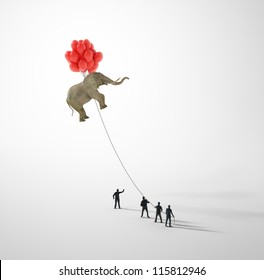 Elephant lifted by balloons and held on a rope by tiny people