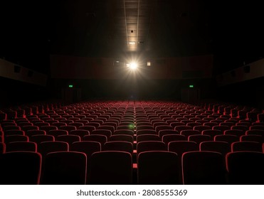 An empty cinema theater with rows of red seats facing a brightly lit stage and spotlight.