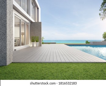 Empty Outdoor Wooden Floor Terrace Near Swimming Pool And Green Grass Garden In Modern Beach House Or Luxury Villa. Building Exterior 3d Rendering With Sea View.