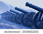 An evocative array of vintage cannons from a bygone military era, meticulously arrayed on an ancient cobblestone path, shrouded by a somber overcast ambiance.