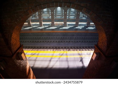 An evocative composition highlights the contrasting textures and forms as sunlight streams through an arched window, offering a voyeuristic view of a busy railway platform below filled with commuters.