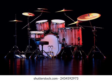 An expansive drum kit with various drums, cymbals, and drumsticks, all under moody stage lighting ready for a dynamic musical performance or studio recording. - Powered by Shutterstock