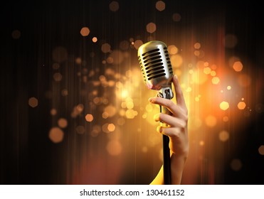 Female hand holding a single retro microphone against colourful background - Powered by Shutterstock