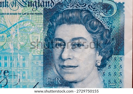 A five pound note displays the portrait of Queen Elizabeth. The note has details in blue and shows security features. It is a form of currency used in the United Kingdom.