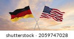 flags of Germany and United States of America waving in the wind on flagpoles against sky with clouds on sunny day. Symbolizing relationship, dialog between two countries. 3d illustration,