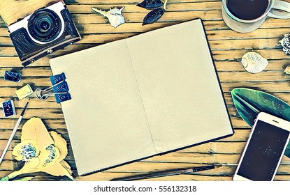 Flat lay composition in vintage style. Open notebook with blank page. Yellow toned background. Retro photo camera, smartphone with black screen, coffee cup, tropical flower, sea shell. Travel banner