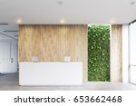 Front view of a white reception desk with two laptops standing on it in front of a wooden office wall. There is a grass wall seen through a wall opening. 3d rendering, mock up