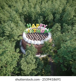 giant birthday cake with colorful Happy Birthday letters on top, placed in the middle of a lush green forest, creating a playful and surreal outdoor celebration scene. 3d render - Powered by Shutterstock