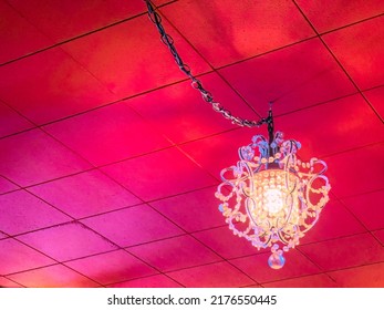Glowing Electric Light Fixture Of Ornamental Glass Hanging Like A Chandelier From Red Ceiling Of Urban Restaurant. Digital Painting Effect, 3D Rendering.