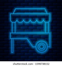 Glowing neon line Fast street food cart with awning icon isolated on brick wall background. Urban kiosk.  