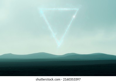 A graphic design concept of a glowing triangle floating in the sky. Above a bleak moody landscape of distance mountains rising from moorland.