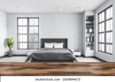 Grey Living Room Blurred With Wooden Desk On Foreground With Marble Floor, Bed And Grey Linens. Light Grey Minimalist Bedroom With Shelves And Books. Windows With City View, No People 3D Rendering