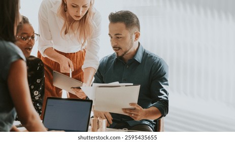 Group of diverse colleagues collaborating, reviewing documents, and discussing ideas in a bright office setting, fostering teamwork and productivity. Business and technology image.