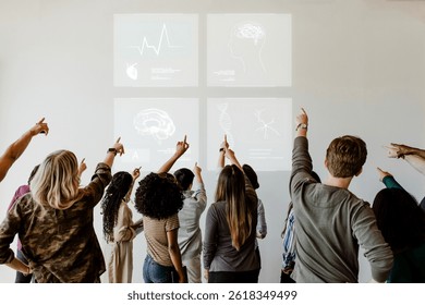 Group of diverse people pointing at medical diagrams on a wall. Mixed gender and ethnicity. Focus on teamwork and learning. Engaged in a collaborative environment. Business image.