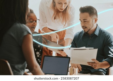 Group of diverse professionals collaborating at a table, reviewing documents and using a laptop, in a modern office setting, teamwork and discussion. Creative business people in casual meeting.