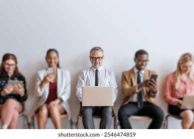 Group of diverse professionals using technology. Middle-aged business man with laptop, others with phones. Business attire, diverse ethnicities, technology focus. Diverse business meeting concept. - Powered by Shutterstock