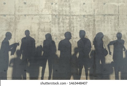 Group Of People Walking In A Relaxed Pose Cast A Shadow On The Concrete Wall. Conceptual Creative Illustration With Silhouettes Of Men And Women. Copy Space. 3D Rendering.