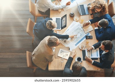 Group of professionals collaborating at a table with laptops, documents, and coffee. Teamwork and discussion in a modern office setting. Overhead view. Business and technology image.