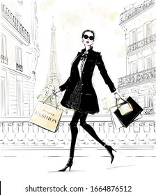 Hand drawn beautiful young woman with bags. Fashion look. Stylish girl in fashion clothes with Paris street background. Woman in black coat. Sketch. Fashion illustration.