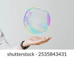 A hand offer a colorful, iridescent bubble against a plain background. The blank rainbow bubble on hand with plain background with copy space for business offering, presentation concept.