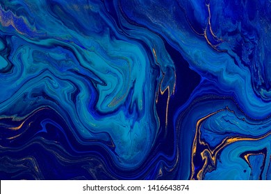 Hand painted background with mixed liquid blue and golden paints. Classic blue color of the year 2020. Abstract fluid acrylic painting. Marbled blue abstract background. Liquid marble pattern