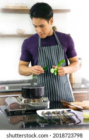 Handsome Chef Prepares Ingredients To Cook Shrimp Soup In Hot Pot At Home Kitchen. Young Man Takes Leisure Time Quarantine Cooking Thai Spicy Food For Dinner. Tom Yam Kung Is A Favorite Dish For All.