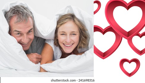 Happy middle aged couple under the duvet against pink hearts - Powered by Shutterstock