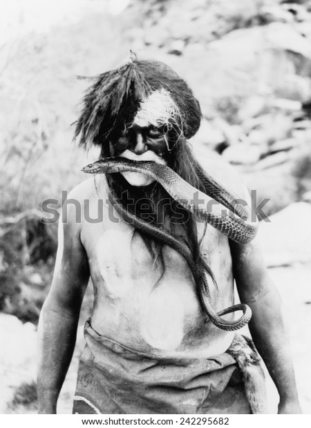 Hopi Indian with painted face and\
body and snake in mouth. Photo by Ralph Murphy,\
1924.