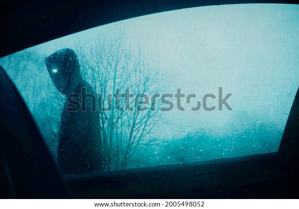 A horror concept. Looking up\
through a car window at a scary supernatural entity with glowing\
eyes, walking past a car. On a moody winters\
evening.